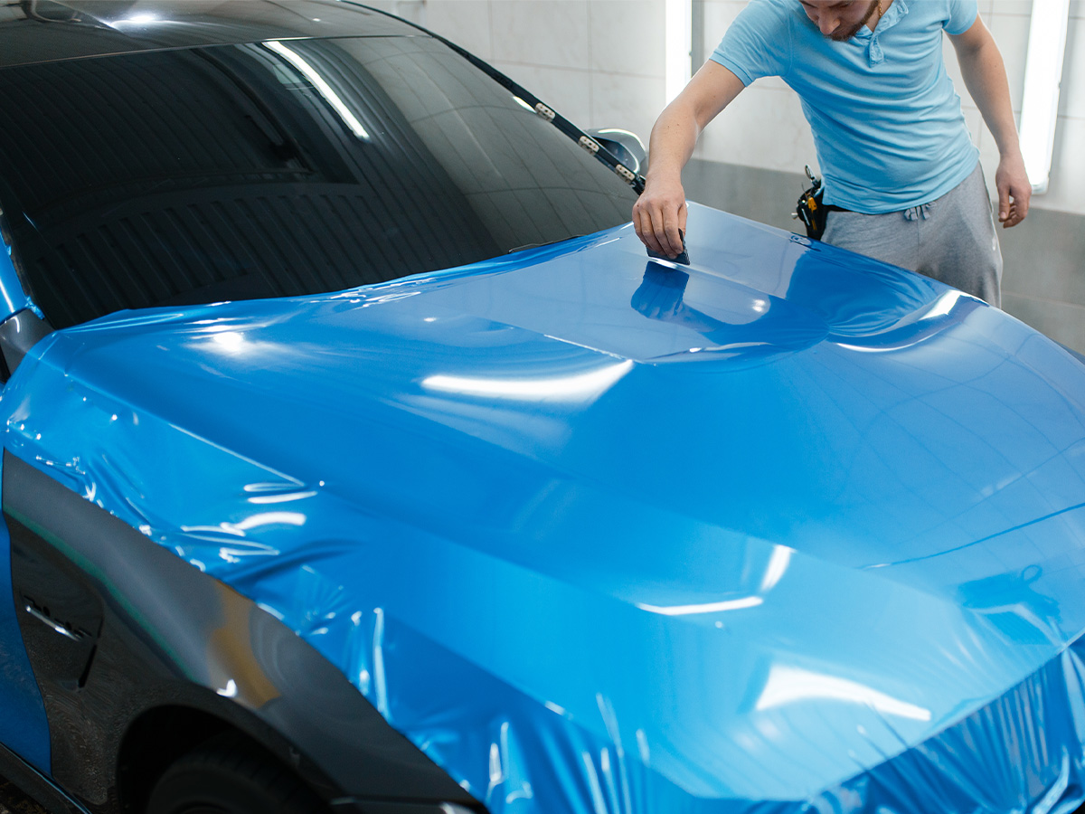 Car wrapping, man with squeegee installs protective vinyl foil or film on hood